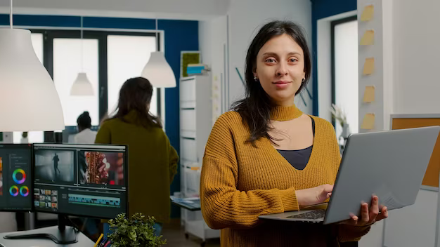 Smiling woman holding laptop in hands against office background