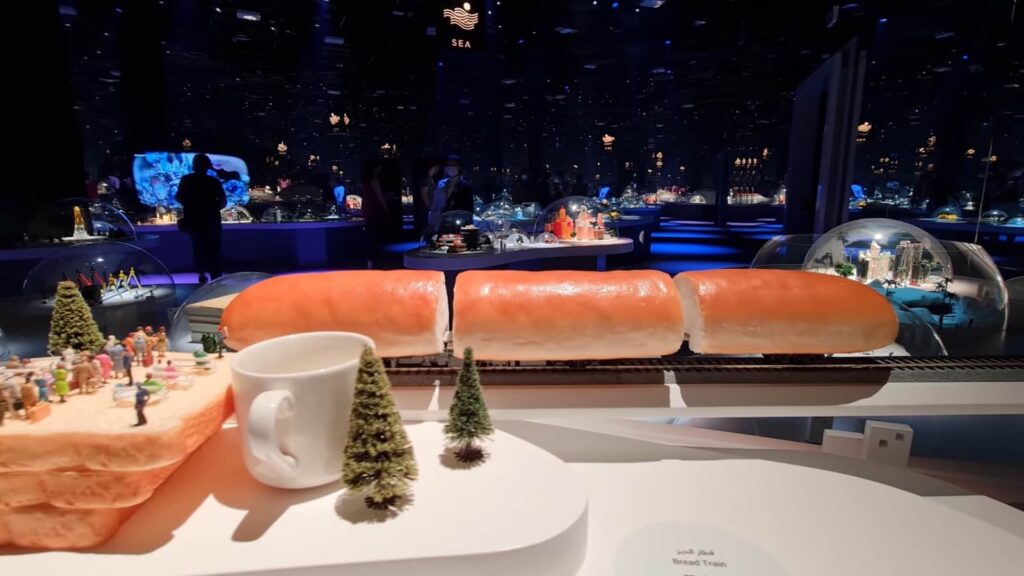 A model train passing through oversized sandwich loaves on a display table