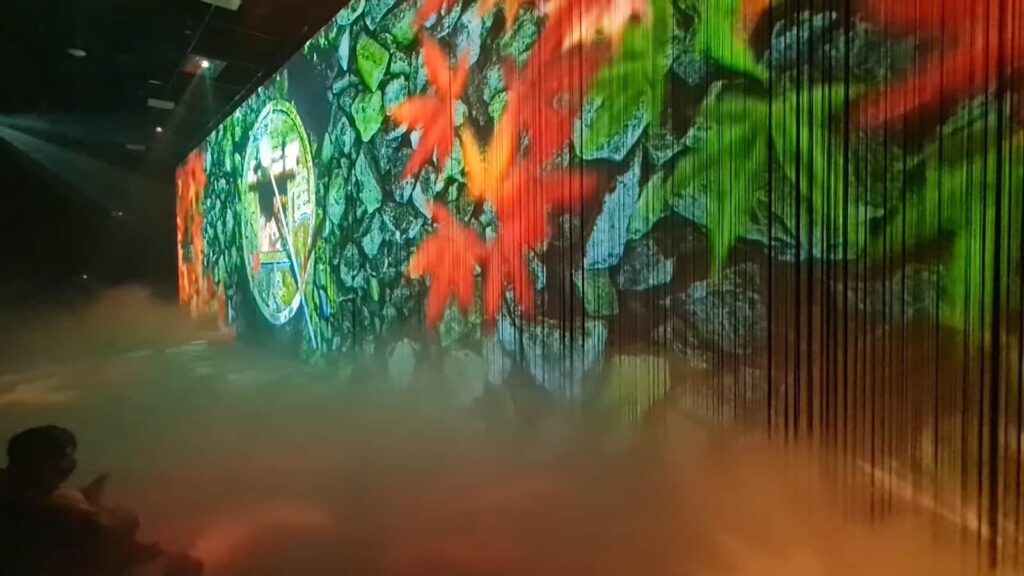 People watching a vibrant, projected wall art with a misty floor